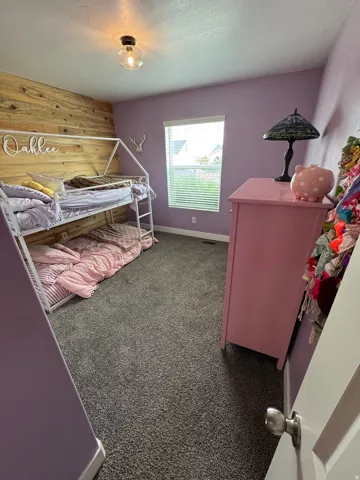 Bedroom featuring a wood-finish accent wall, window with blinds, and gray carpeting