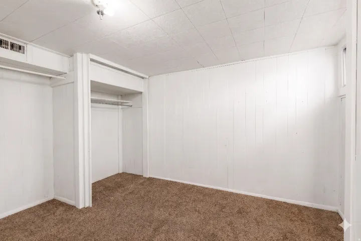 Room featuring white vertical paneling, brown carpeting, and a drop ceiling