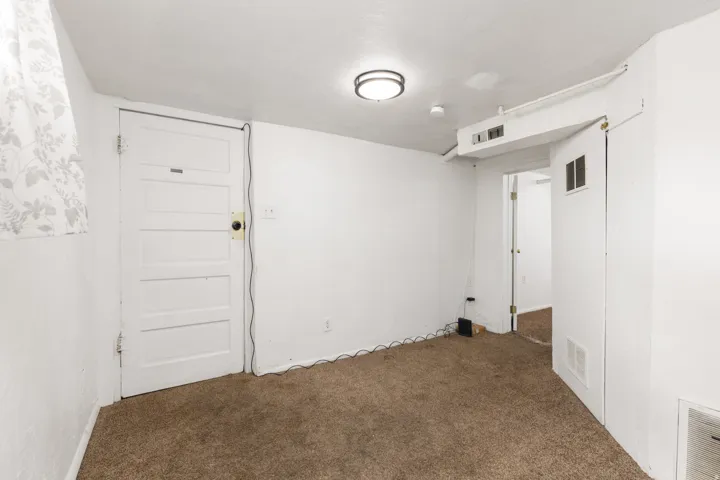 Carpeted room featuring a ceiling-mounted light fixture, white walls, and a window with a patterned curtain