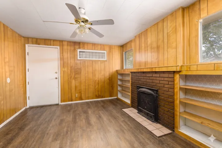 Living space featuring wood-finish wall paneling, a brick fireplace with a tile hearth, and built-in shelving