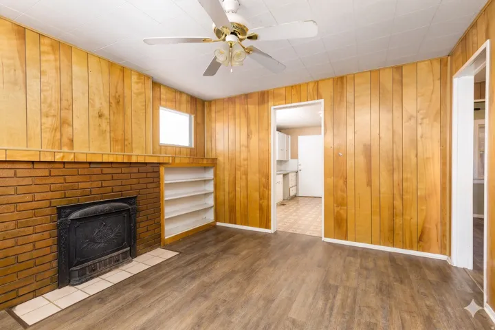 Living area featuring wood-finish flooring, wood paneling, a brick fireplace with a tile hearth, and built-in shelving