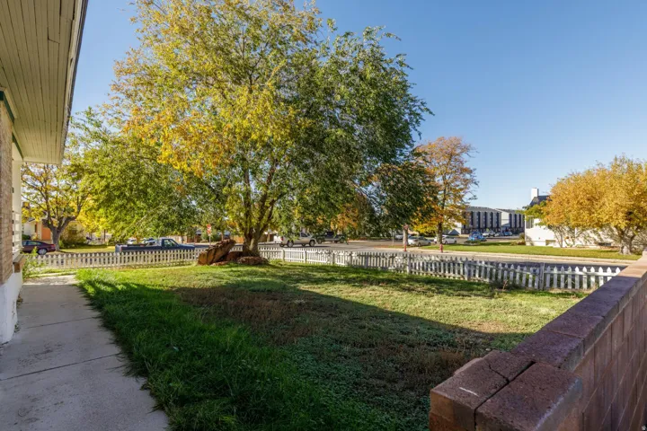 Front yard featuring a picket fence, mature trees, a concrete walkway, and a brick retaining wall