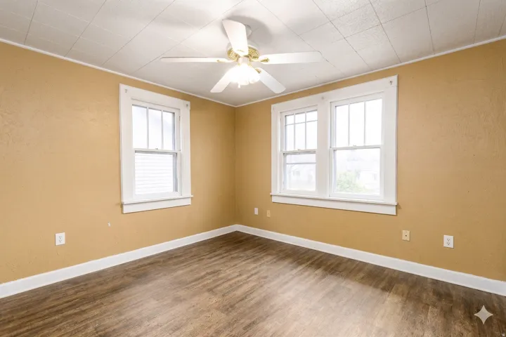 Room featuring wood-finish flooring, two large windows with white trim, and a ceiling fan with integrated lighting