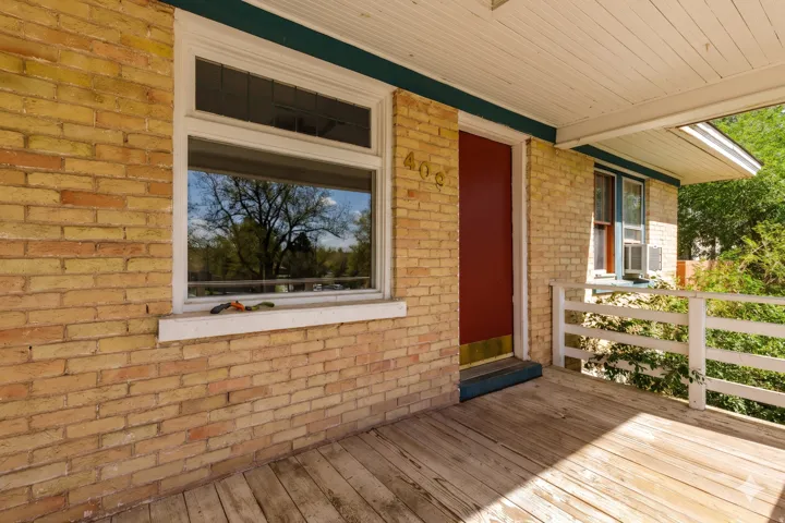 Inviting front porch featuring a red entry door with brass kickplate, light-colored brick exterior, and white wood railing