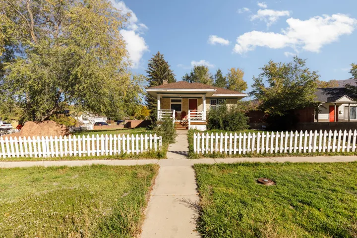 Charming single-story residence featuring a white picket fence, a covered front porch with white railings, and a red entry door