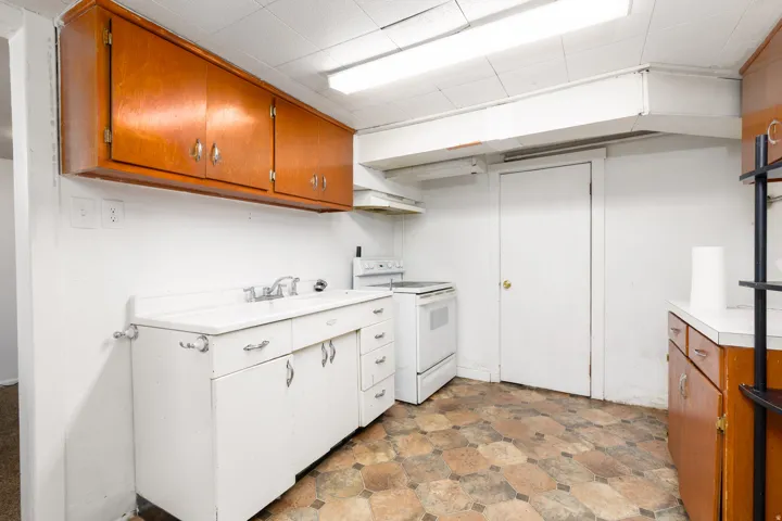 Kitchen area featuring overhead wood-finish cabinetry, a white base cabinet with an integrated sink, a white freestanding range, and octagonal floor tiles