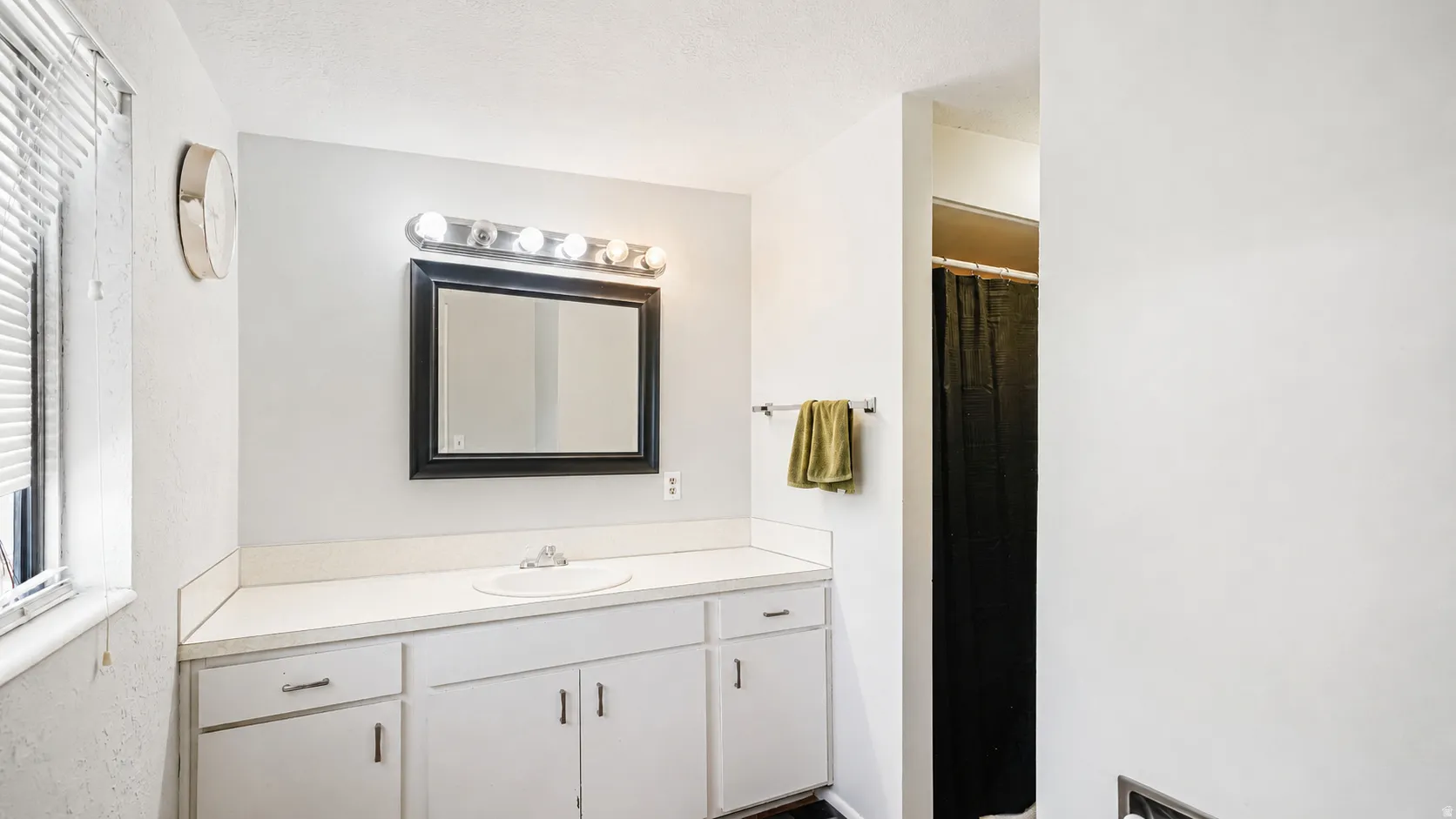 Bathroom featuring a white vanity with an integrated sink, a rectangular mirror with a black frame, and a five-bulb vanity light fixture
