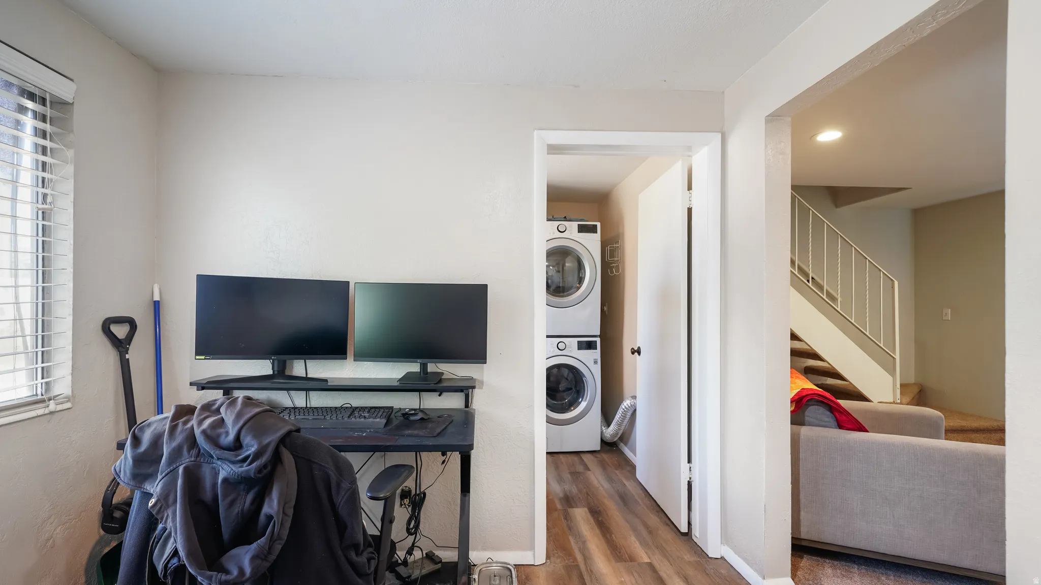 Dedicated laundry area featuring stacked appliances and wood-finish flooring