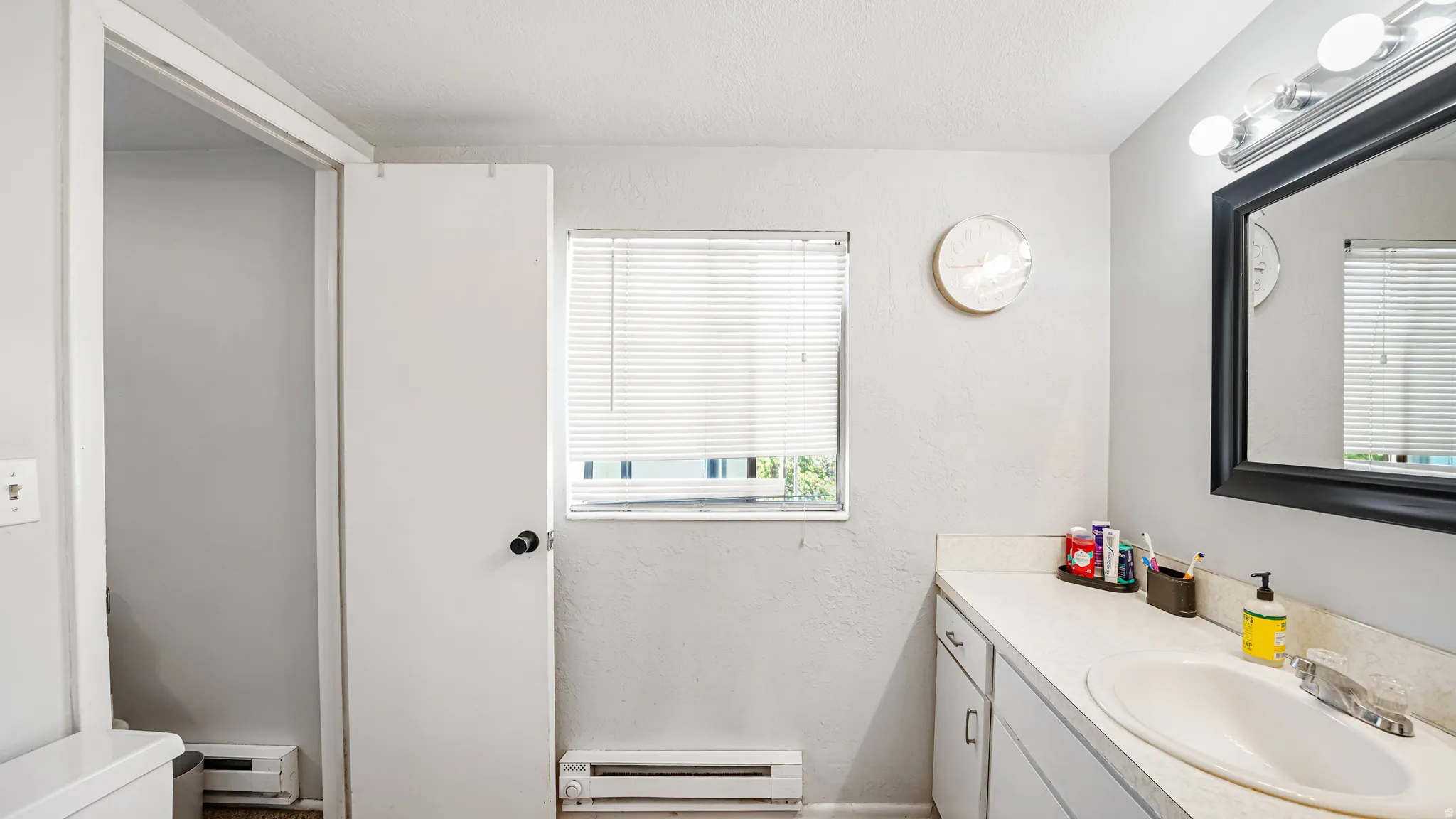Bathroom featuring a single vanity with an integrated sink, a rectangular mirror with a black frame, and a wall-mounted light fixture