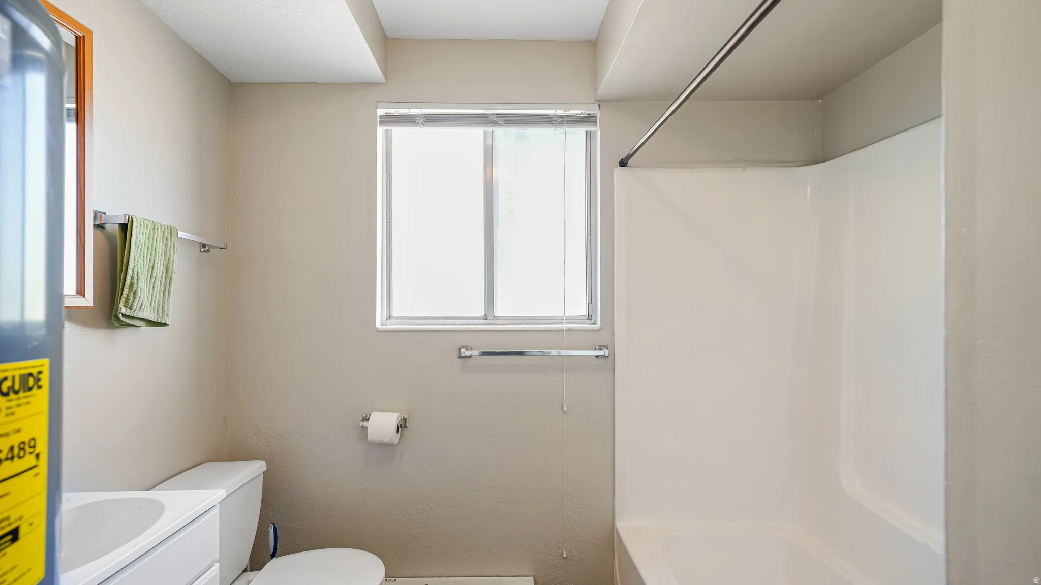 Bathroom featuring a white shower-tub combination, a window with blinds, and a toilet