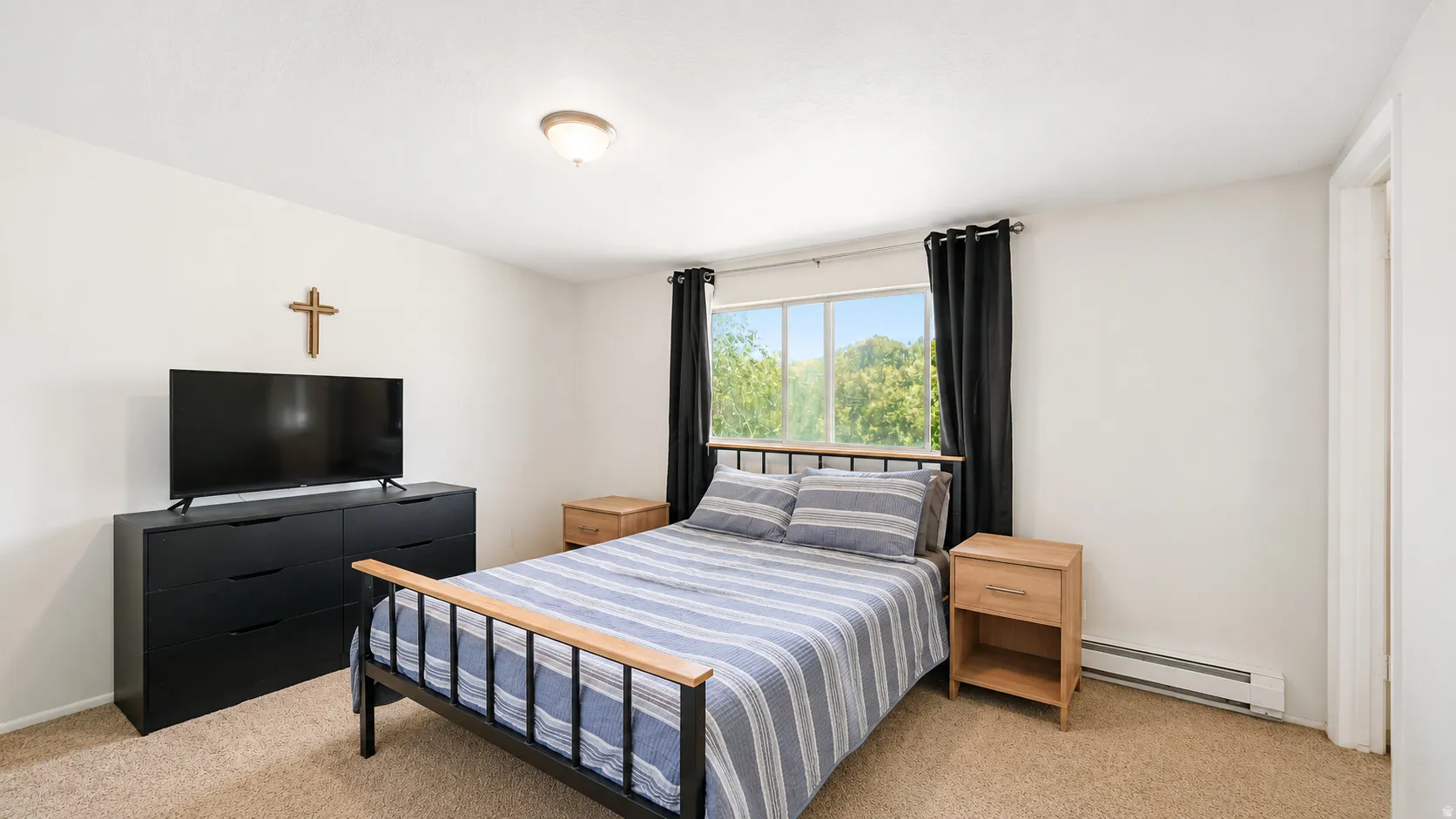 Room featuring a window with exterior tree scenery, light-colored carpeting, white wall paint, and a ceiling-mounted light fixture