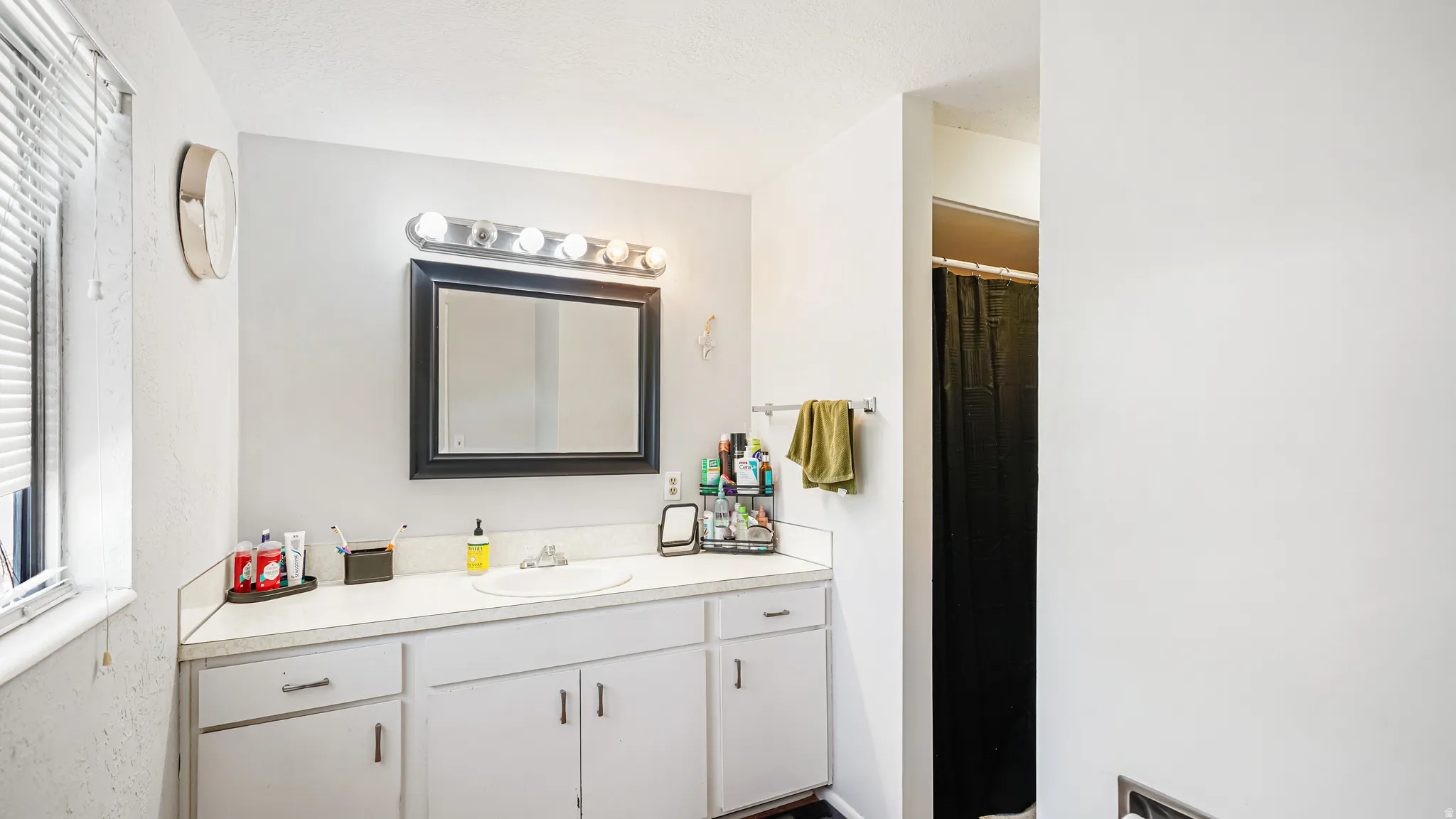 Bathroom featuring a vanity with an integrated sink, ample counter space, white cabinetry with silver hardware, a framed mirror, and overhead lighting