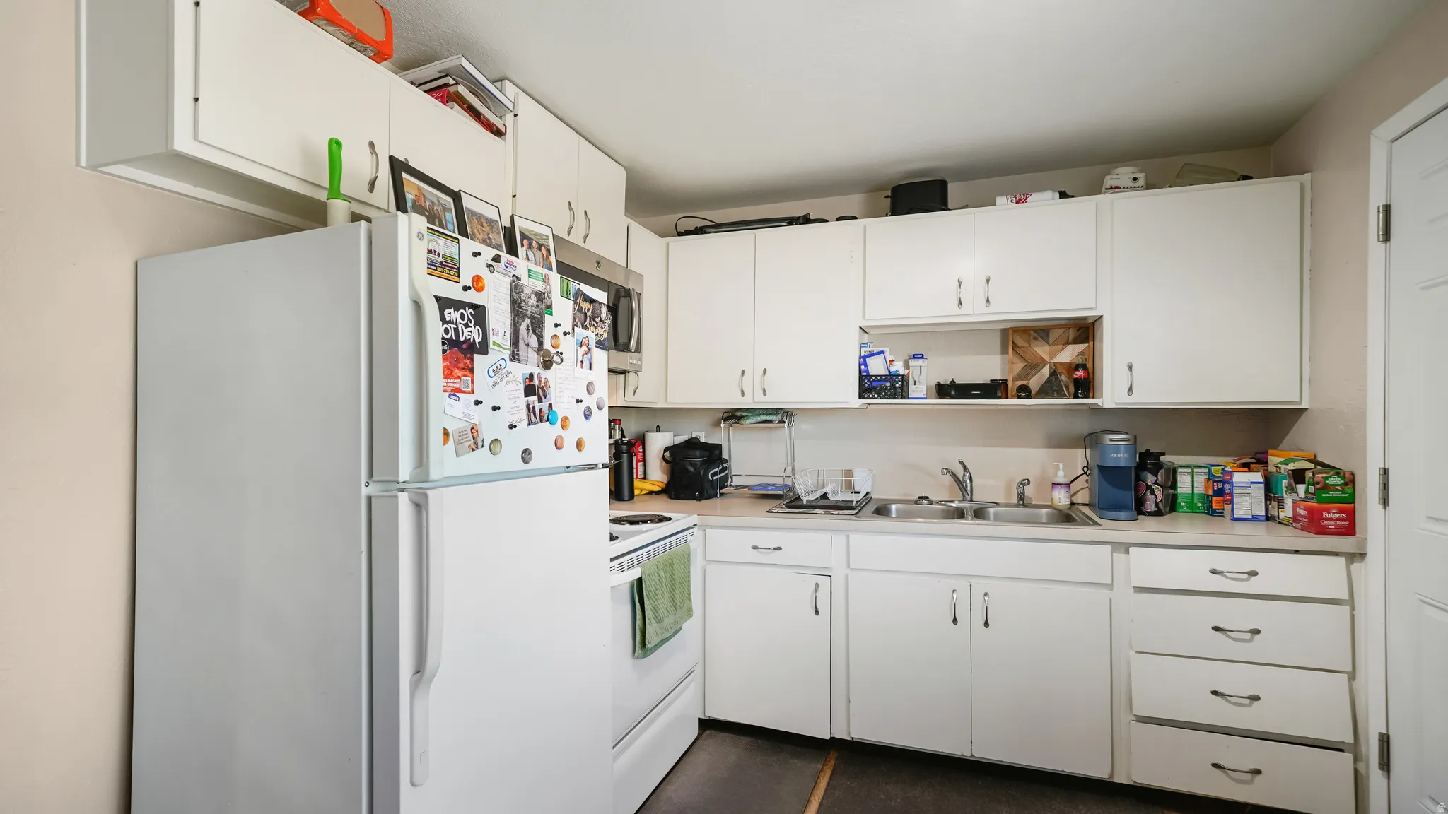Kitchen featuring white cabinetry with ample storage, a stainless steel microwave, a dual-basin sink, and wood-finish flooring