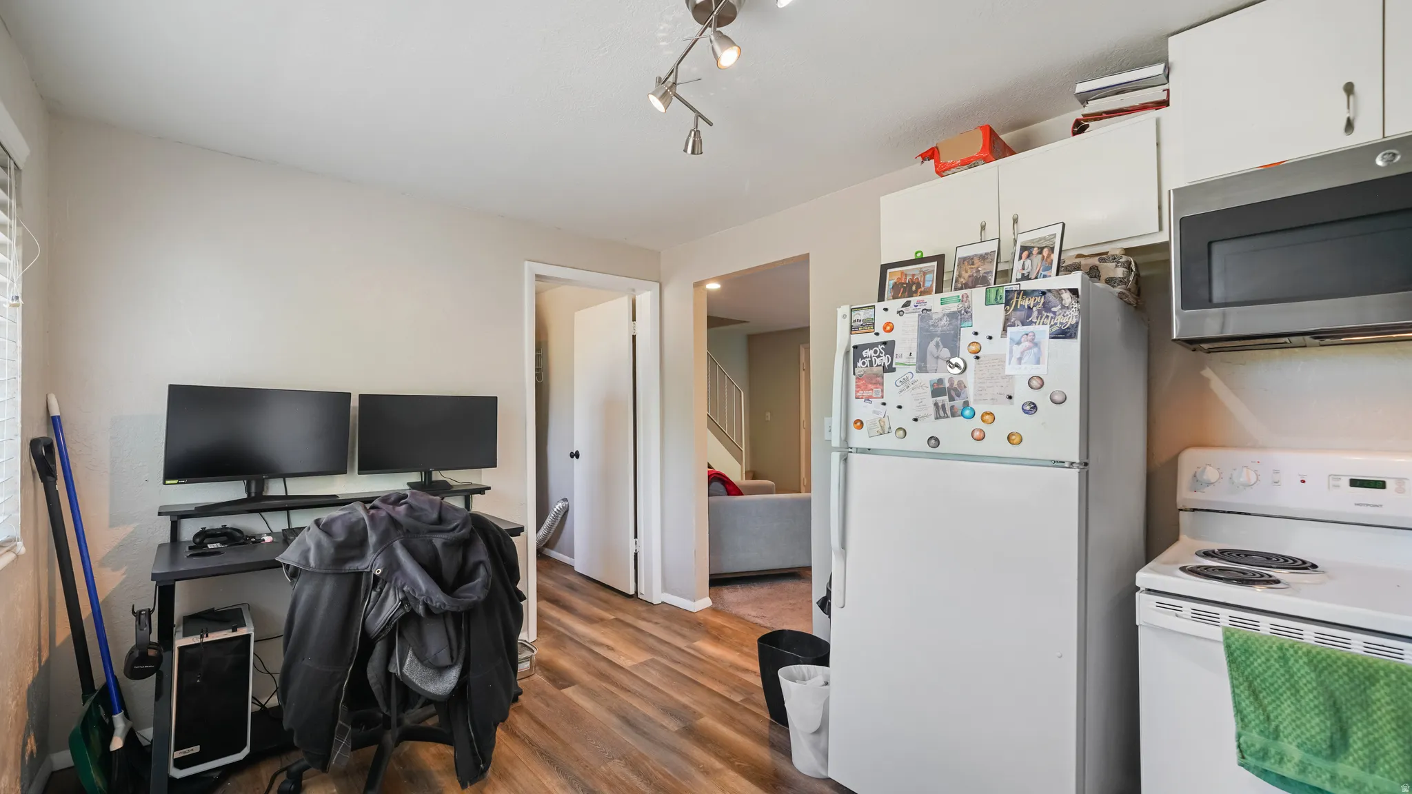 Kitchenette featuring white appliances, upper cabinetry, and wood-finish flooring