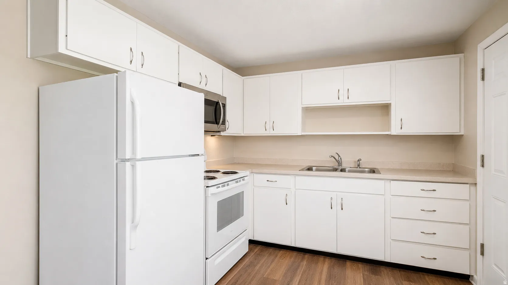 Kitchen featuring white cabinetry, light countertops, wood-finish flooring, a stainless steel microwave, and a white oven