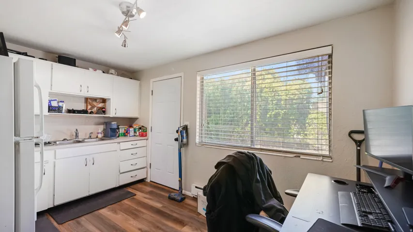 Kitchenette featuring white cabinetry, a stainless steel sink, and wood-finish flooring