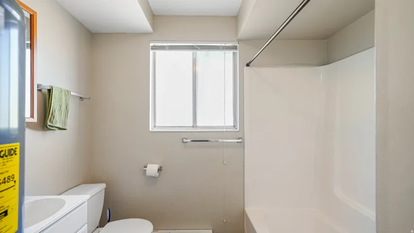 Bathroom featuring a white shower-tub combination, a window with blinds, and a toilet
