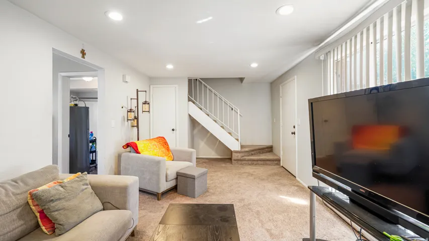Carpeted living space featuring recessed lighting, a white painted staircase, and a large window with vertical blinds