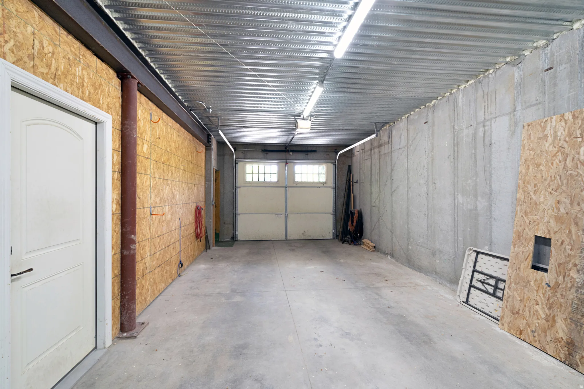 Concrete flooring and walls featuring a corrugated metal ceiling with fluorescent lighting