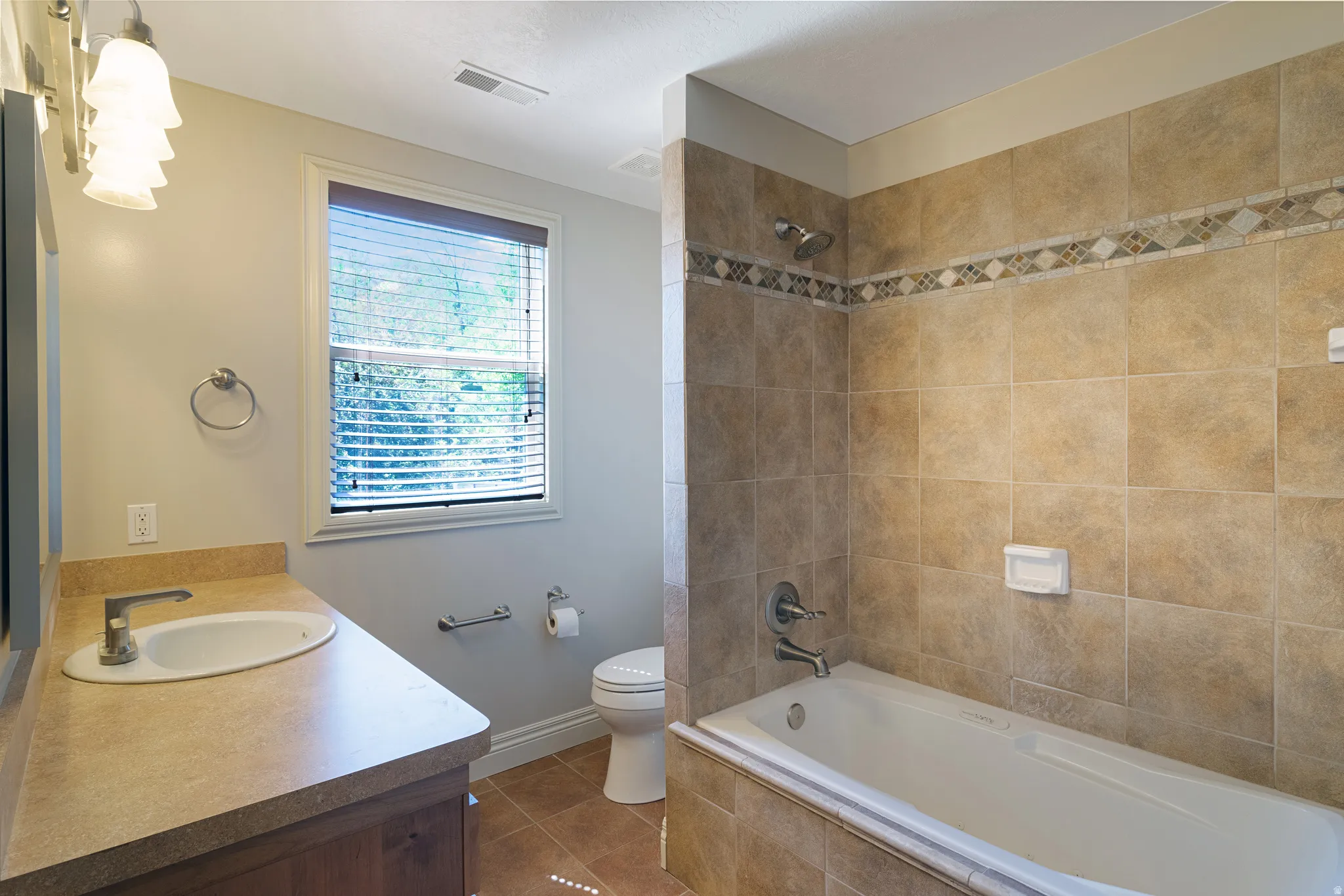 Bathroom featuring a neutral-toned vanity with an integrated sink, a window with blinds, and a tiled shower/tub combination