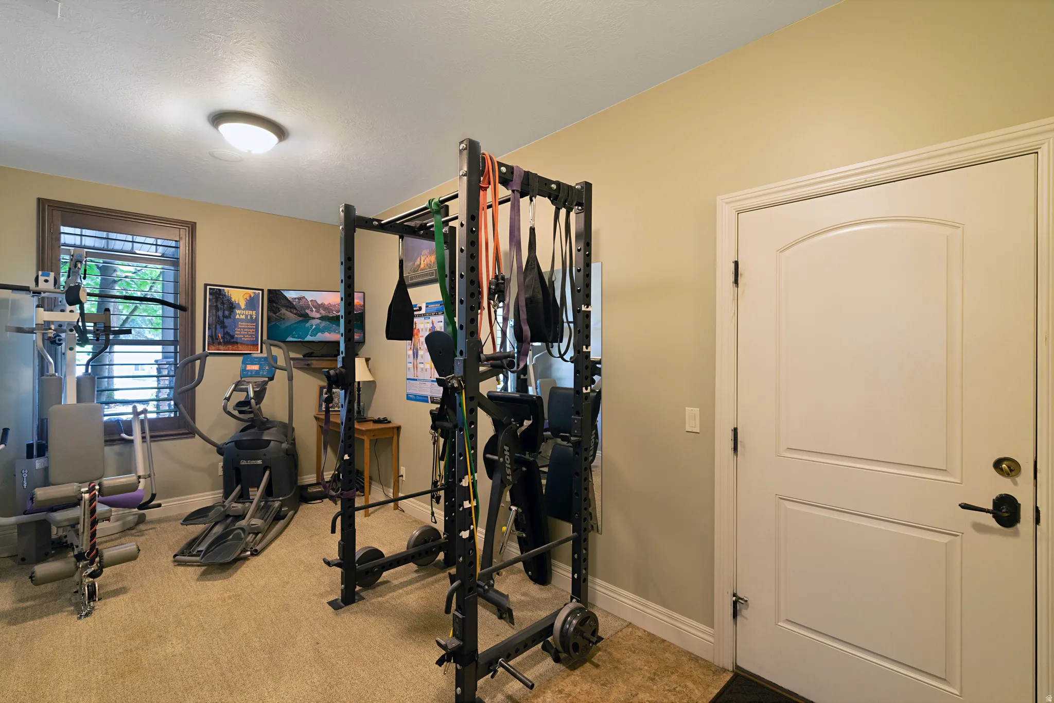 Recessed lighting illuminates a versatile room with carpet flooring, a window featuring horizontal blinds, and a white interior door with an arched panel