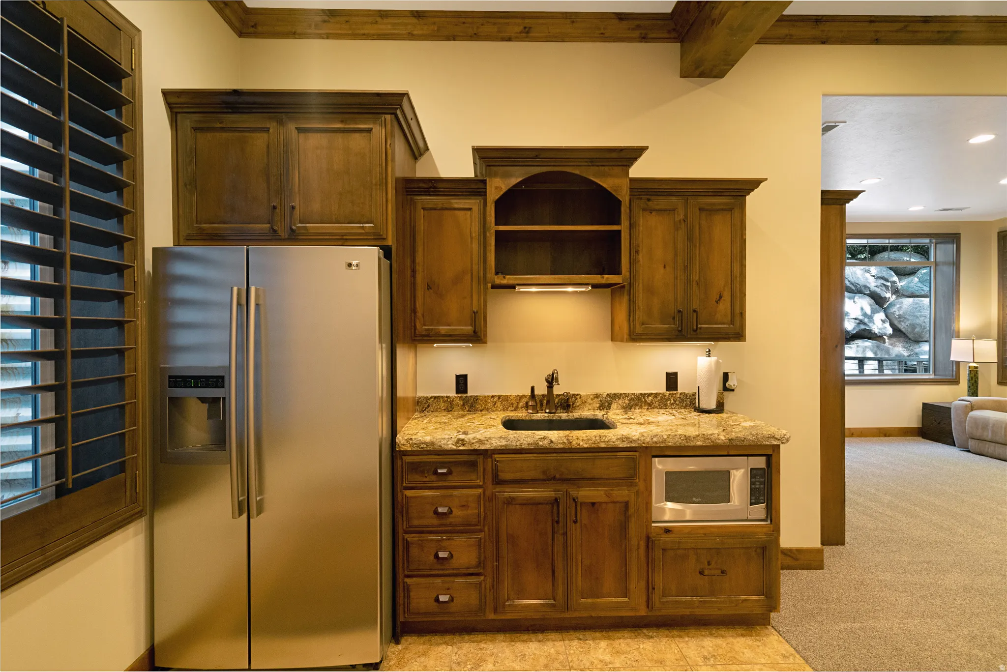 Kitchenette featuring a stainless steel refrigerator, built-in microwave, wood cabinetry, stone-finish countertops, and a sink with a dark-finish faucet