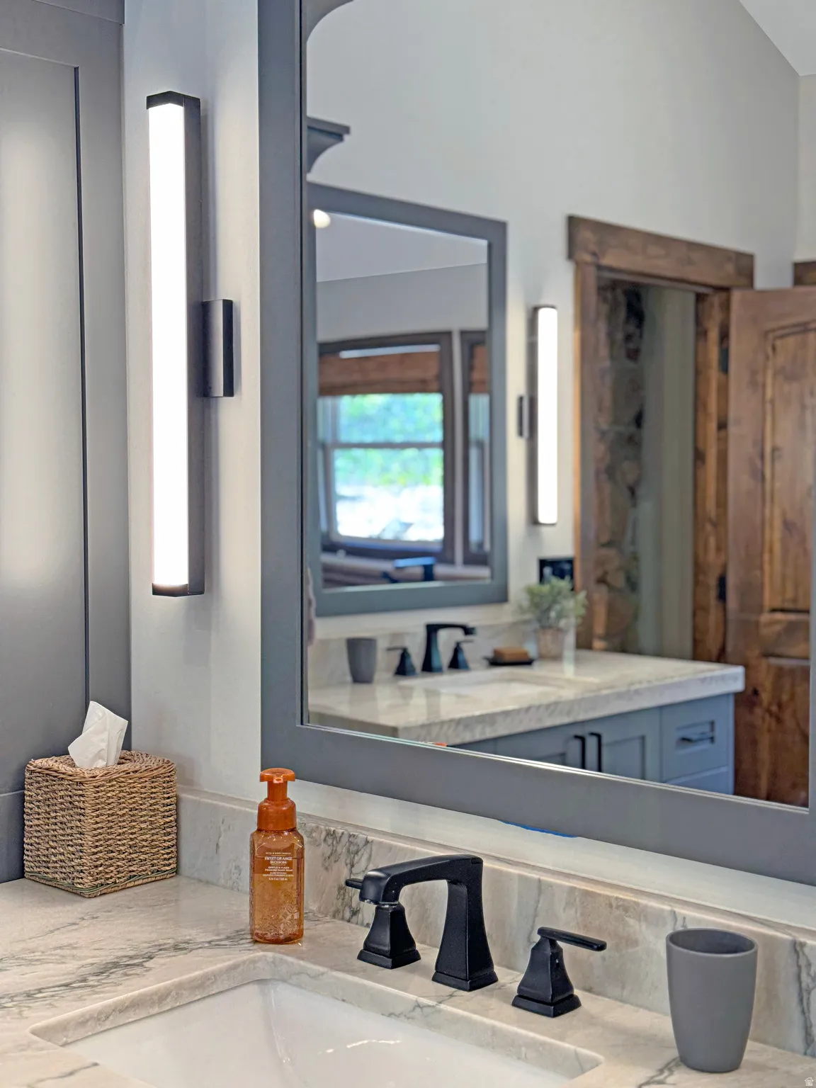Bathroom vanity with a white rectangular undermount sink, a three-piece matte black faucet, and a light-toned stone countertop