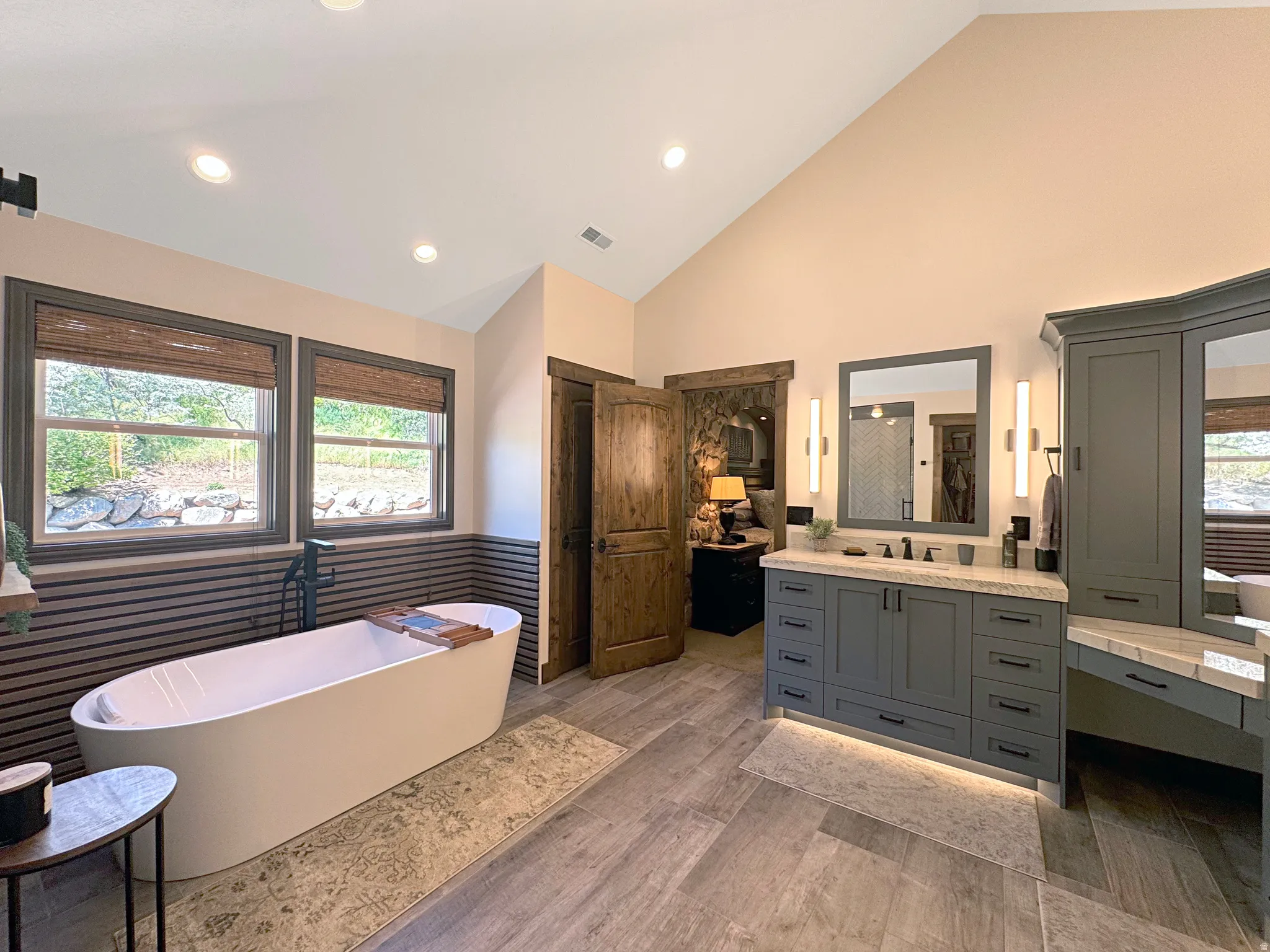 Spacious bathroom featuring a freestanding soaking tub, dual windows, and a vaulted ceiling