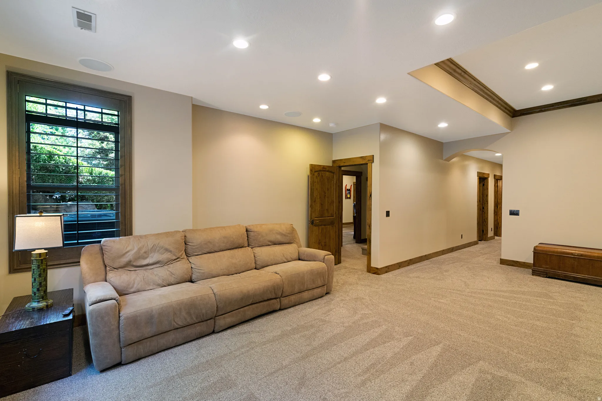 Carpeted recreation area featuring recessed lighting, a decorative wood-trimmed ceiling element, and a window with exterior tree views