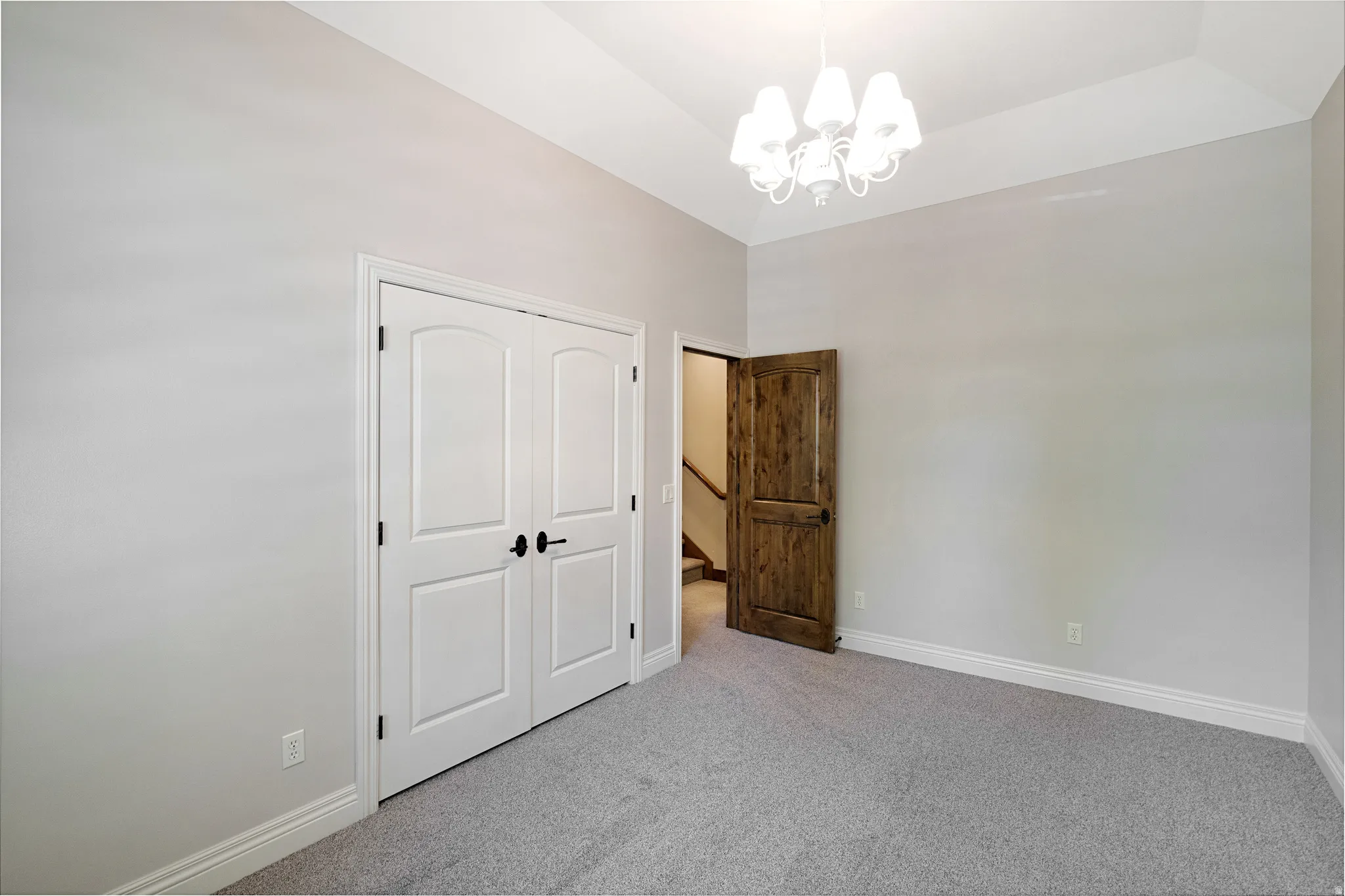 Spacious room featuring vaulted ceilings, light gray wall tones, and plush gray carpeting