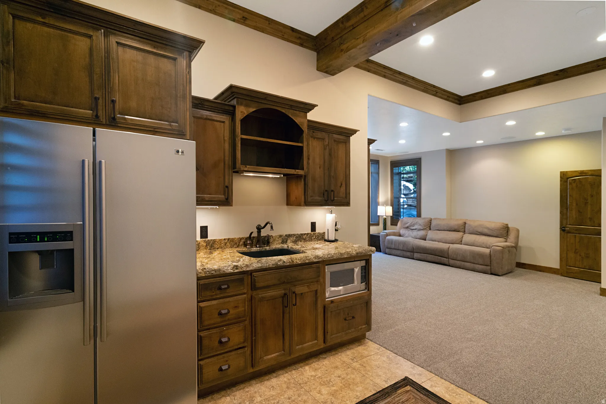 Lower-level living area featuring a wet bar with a stainless steel refrigerator, built-in microwave, and wood-finish cabinetry