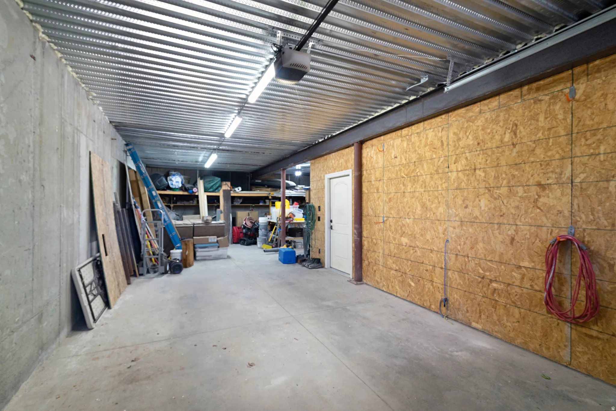 Spacious utility area featuring a concrete floor, exposed corrugated metal ceiling, and fluorescent lighting
