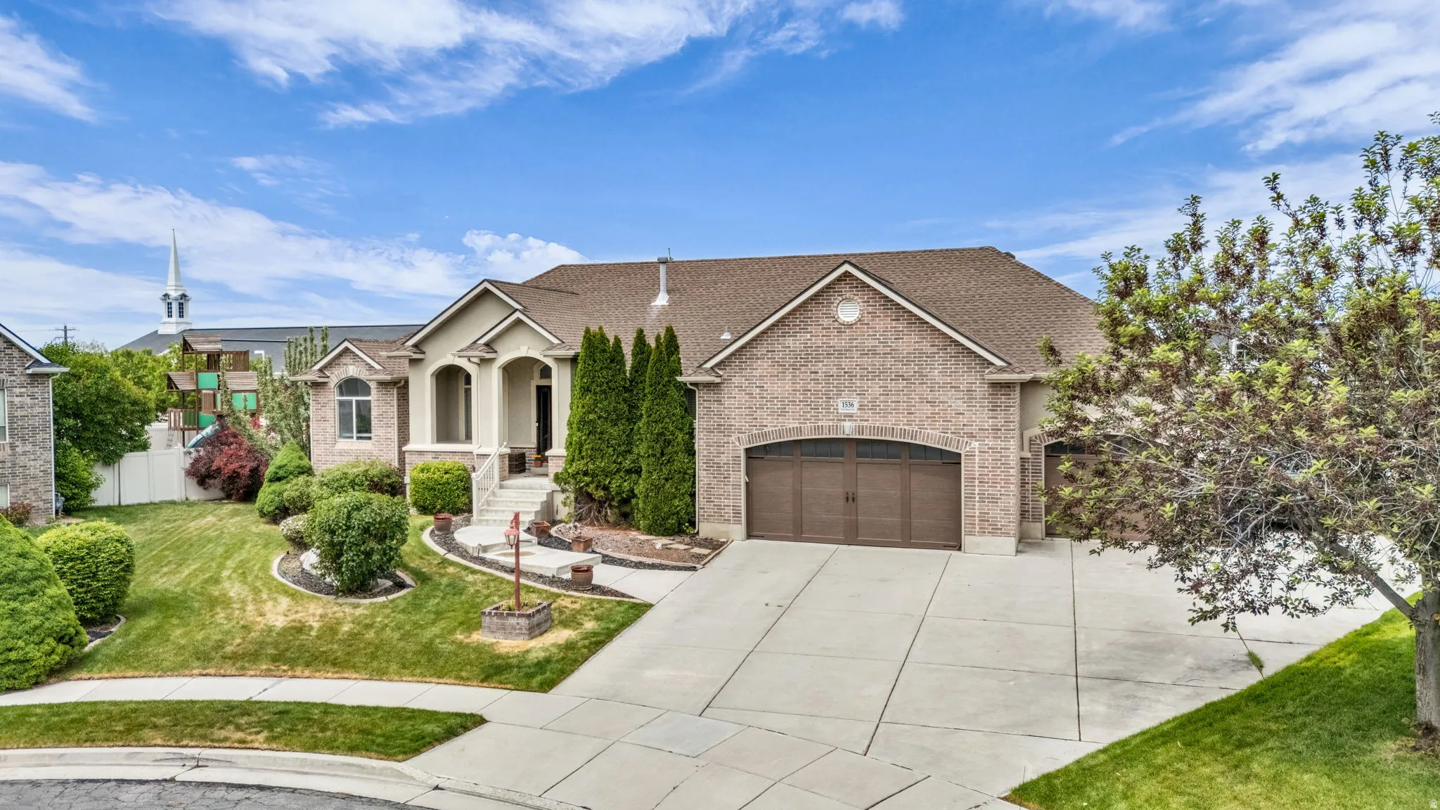 Brick and stucco exterior featuring an arched entryway, two-car garage with wood-finish doors, a concrete driveway, and established landscaping