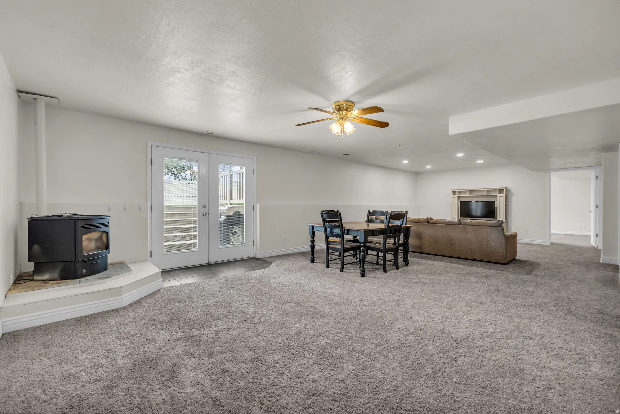 Spacious carpeted room featuring a corner wood-burning stove, white wainscoting, and French doors leading to exterior stairs