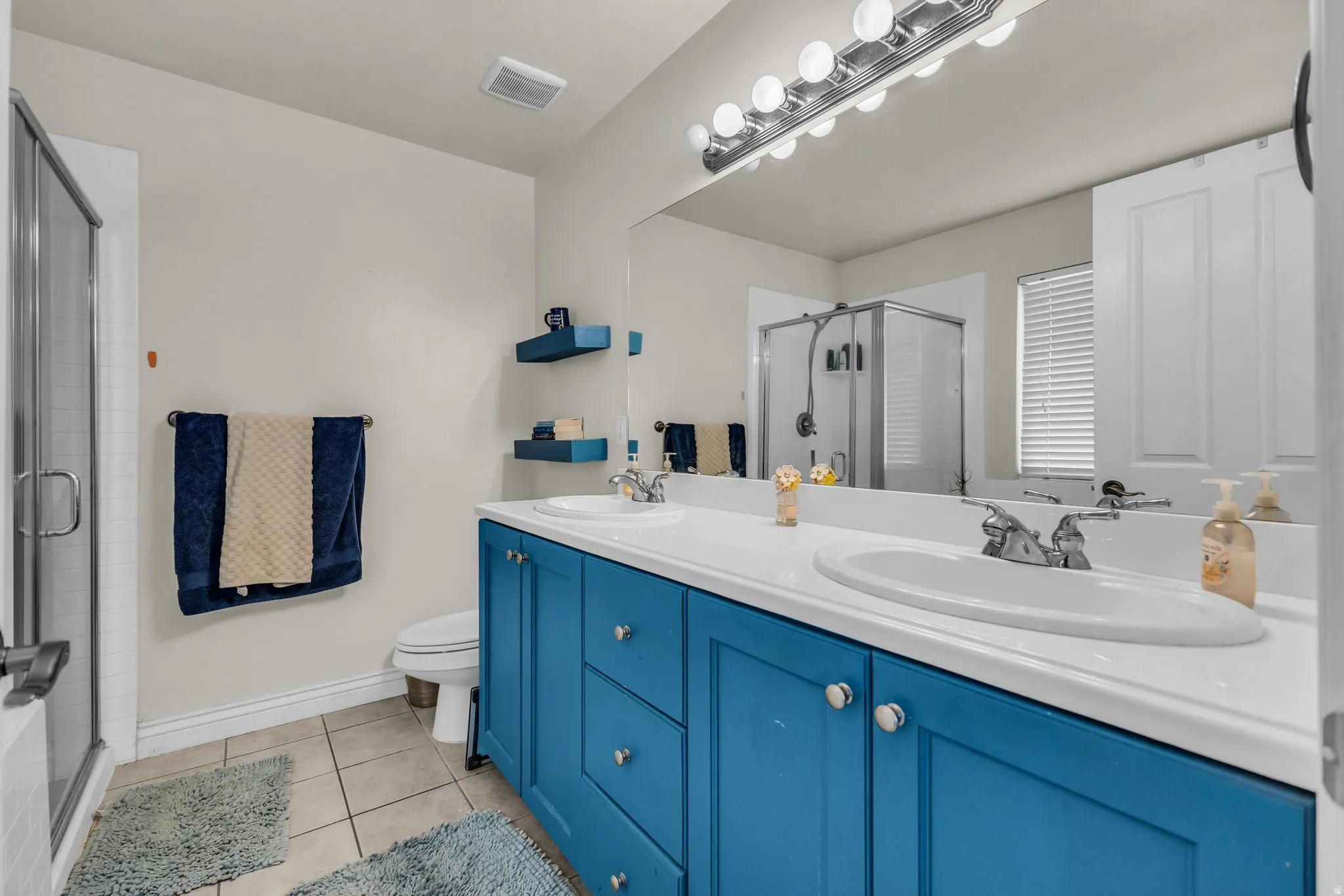 Dual basin vanity with blue cabinetry and chrome hardware, featuring a full-width mirror and polished chrome vanity lighting