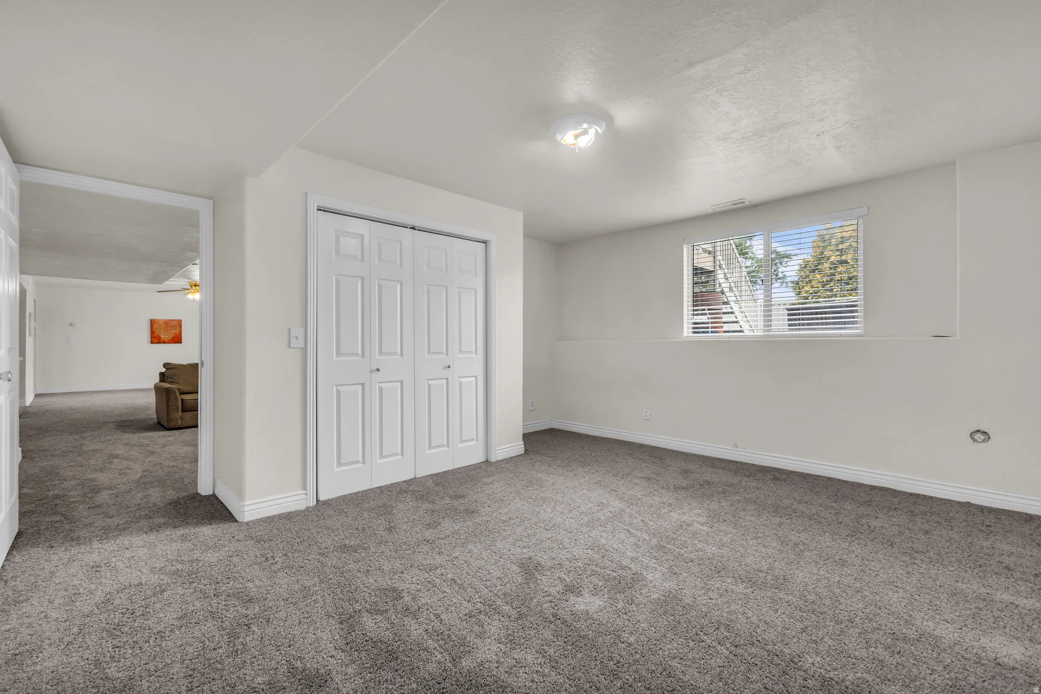 Spacious room featuring neutral carpeting, white walls, a built-in closet with bifold doors, a window with blinds, and recessed lighting