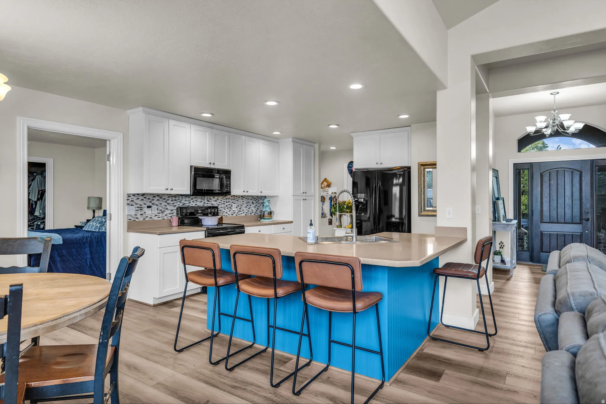 Bright kitchen featuring white cabinetry, a mosaic tile backsplash, black appliances, a central island with a breakfast bar, and wood-finish flooring