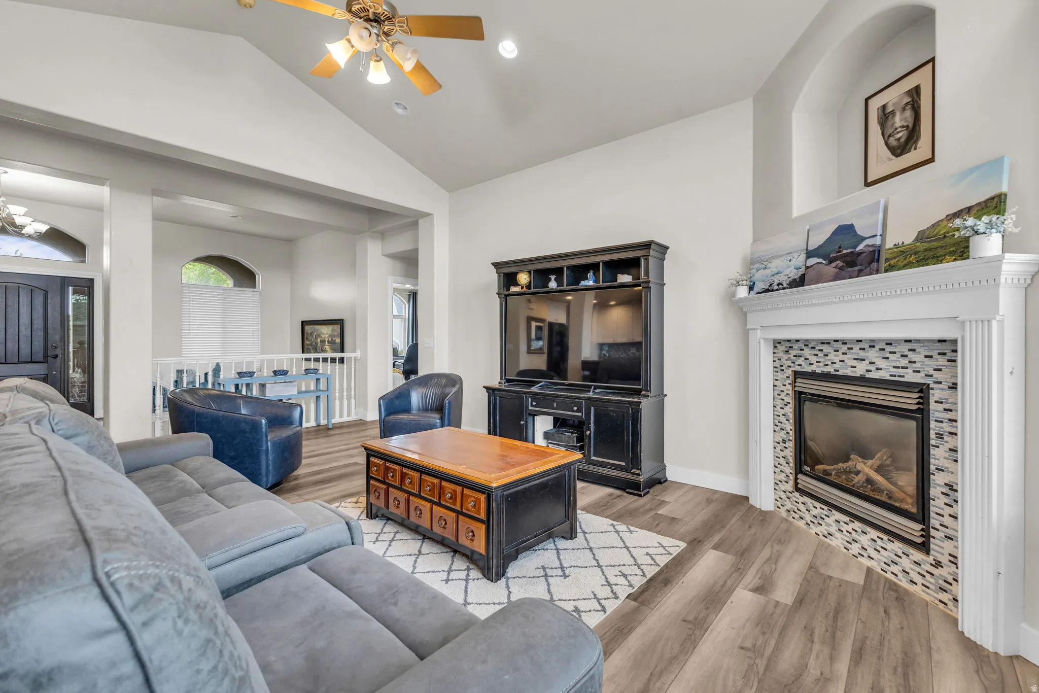Living area featuring a fireplace with mosaic tile surround, a built-in media console, wood-finish flooring, and vaulted ceilings with a ceiling fan