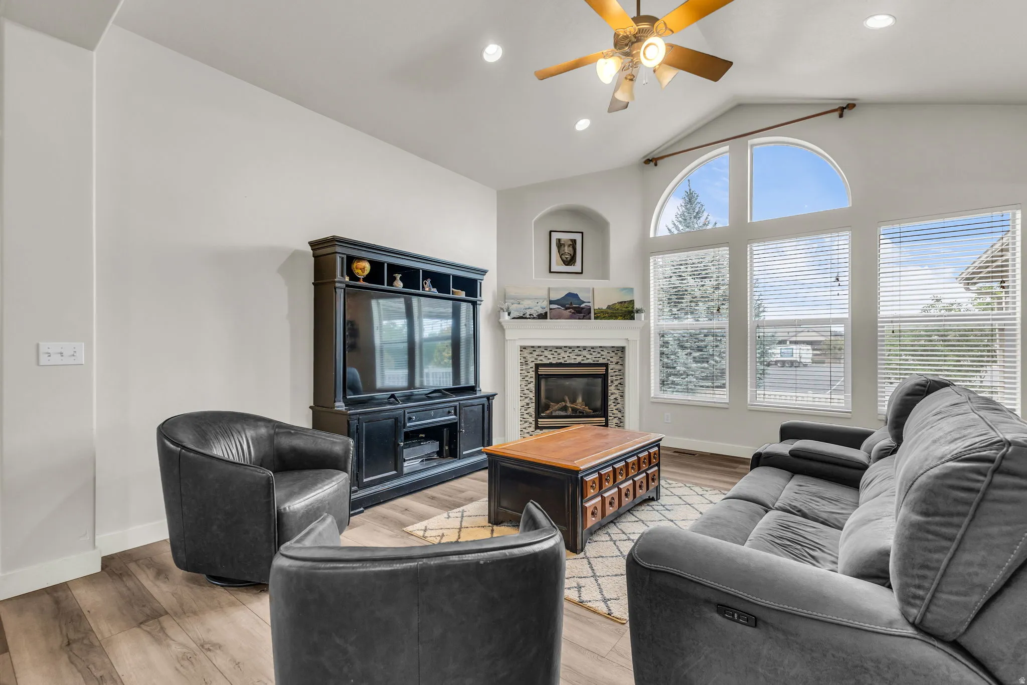 Vaulted ceiling living space featuring wood-finish flooring, a contemporary fireplace with tile surround, and multiple large windows including an arched transom