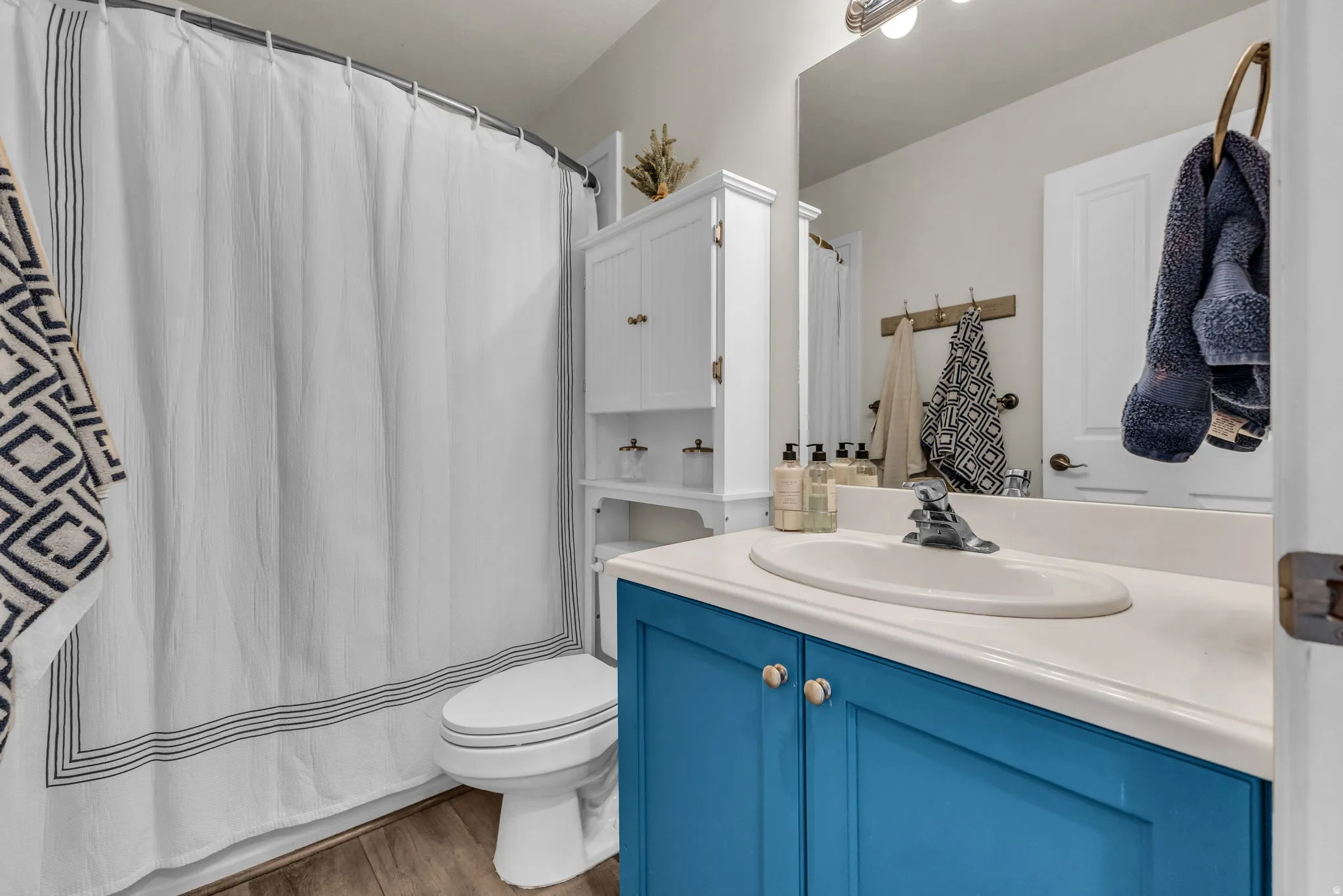 Bathroom featuring wood-finish flooring, a white toilet, and a vanity with a white countertop and blue cabinetry