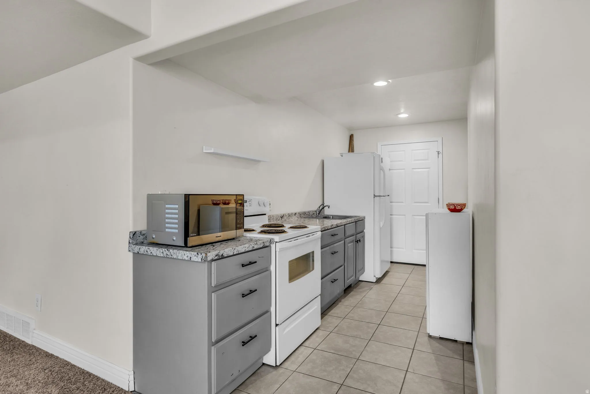 Compact kitchen space featuring light gray cabinetry, speckled countertops, a white electric range, and a white refrigerator