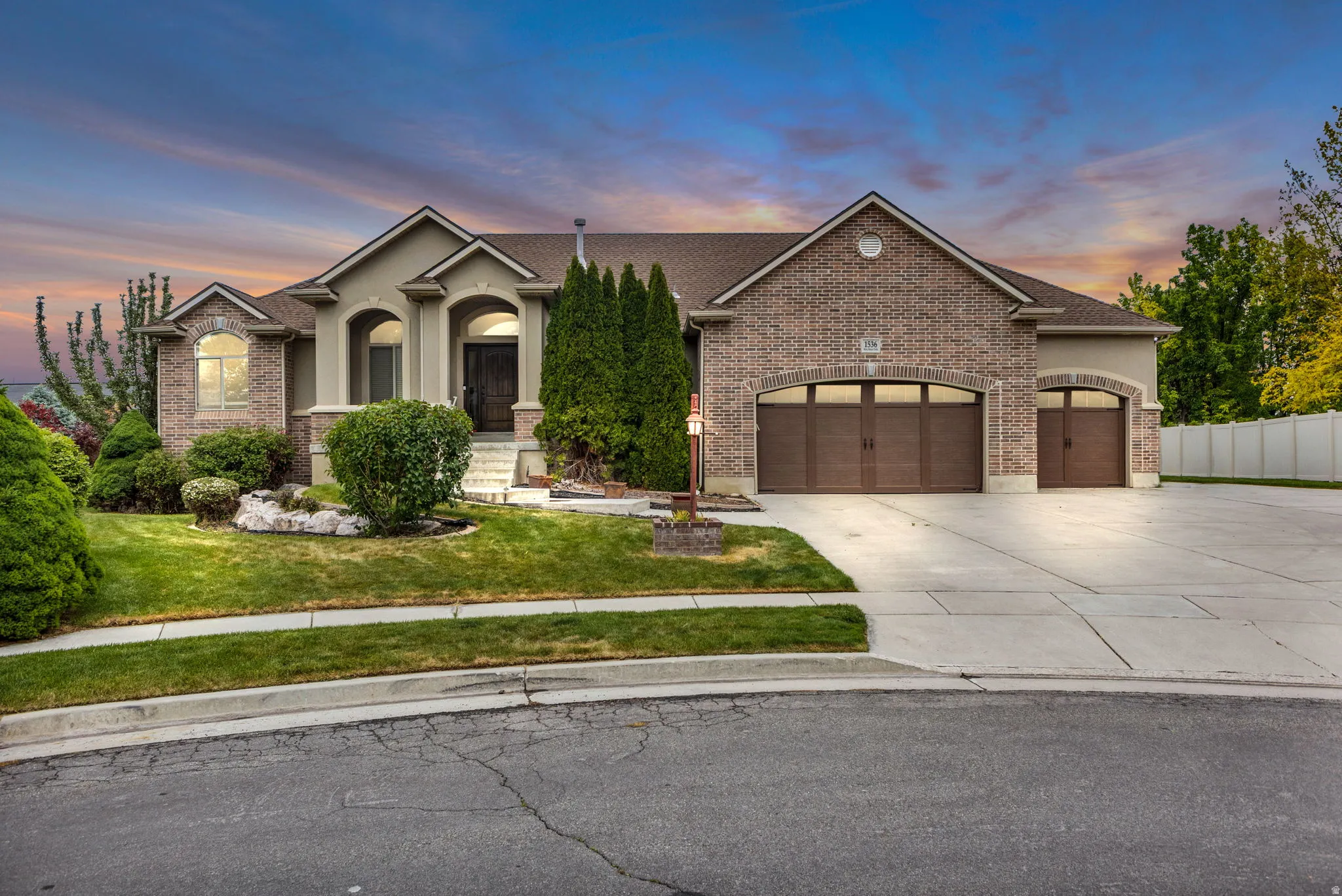 Traditional-style residence featuring a brick and stucco exterior, arched entryways, a multi-car driveway, and mature landscaping