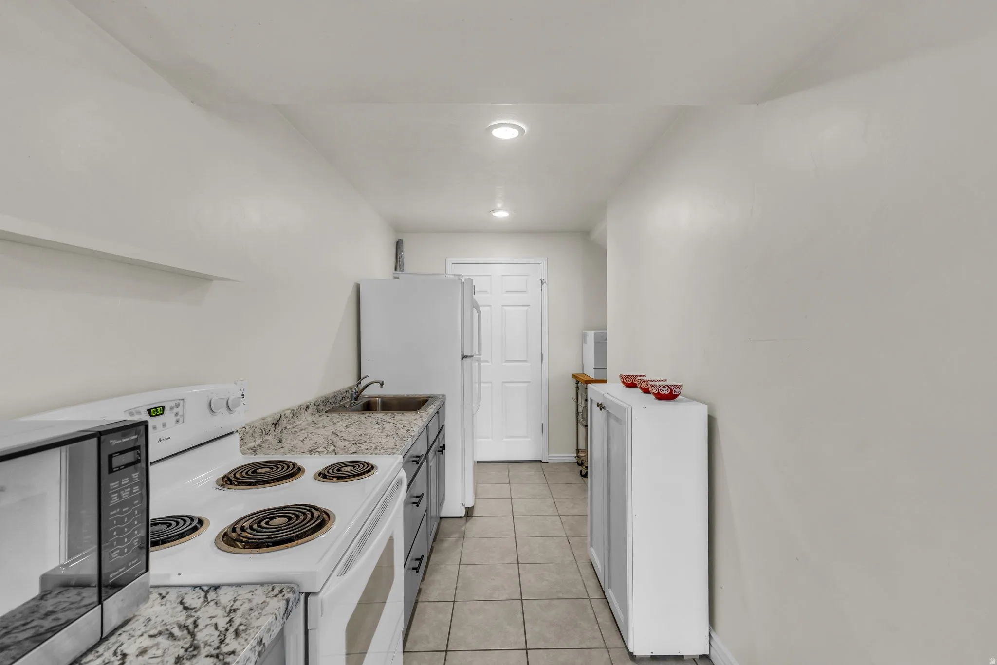 Galley-style kitchen featuring tile flooring, stone-finish countertops, built-in cabinetry, an electric range, and a full-size refrigerator
