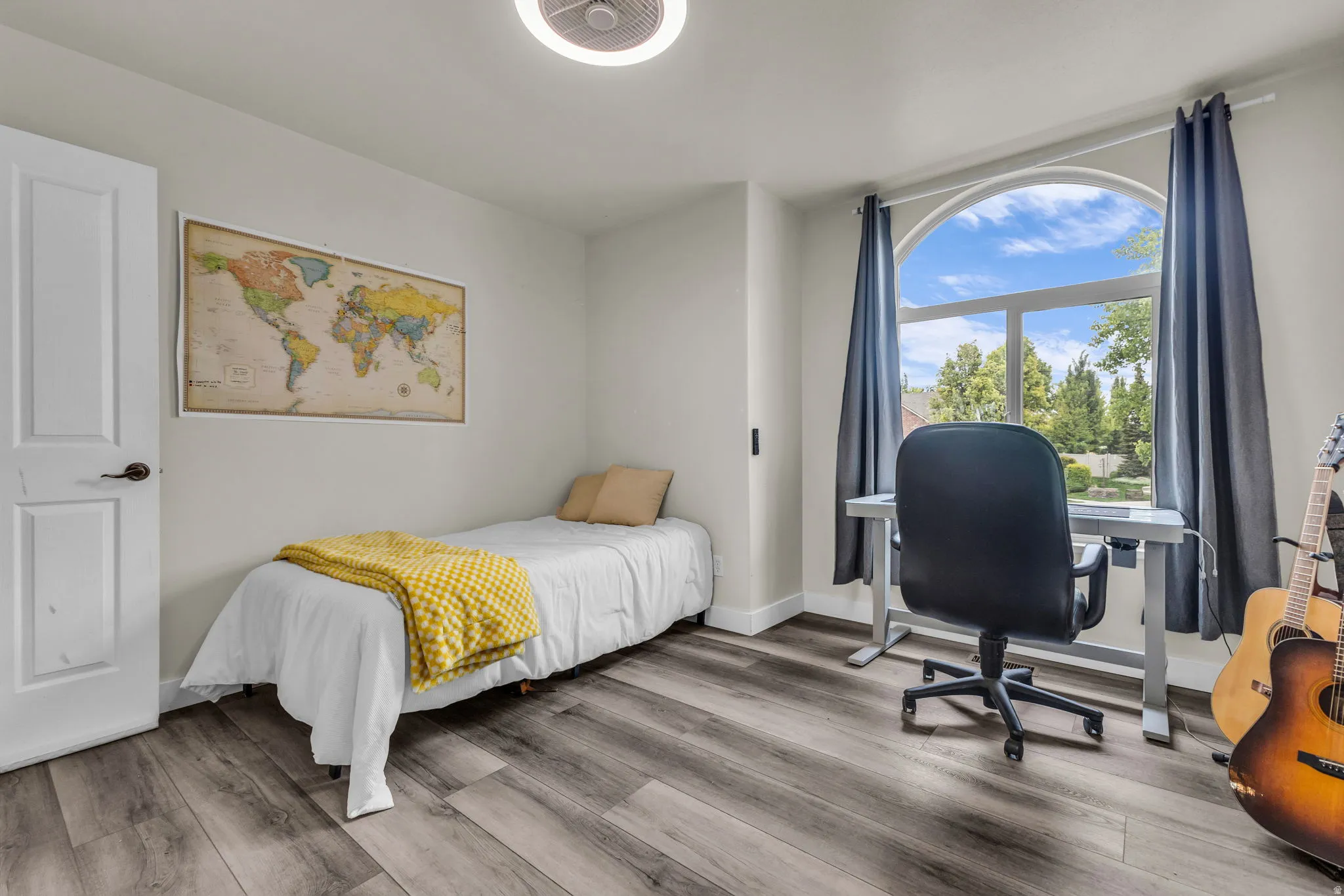 Arch-top window providing natural illumination, wood-finish flooring, white paneled door, light-colored walls, and a ceiling fan with integrated lighting