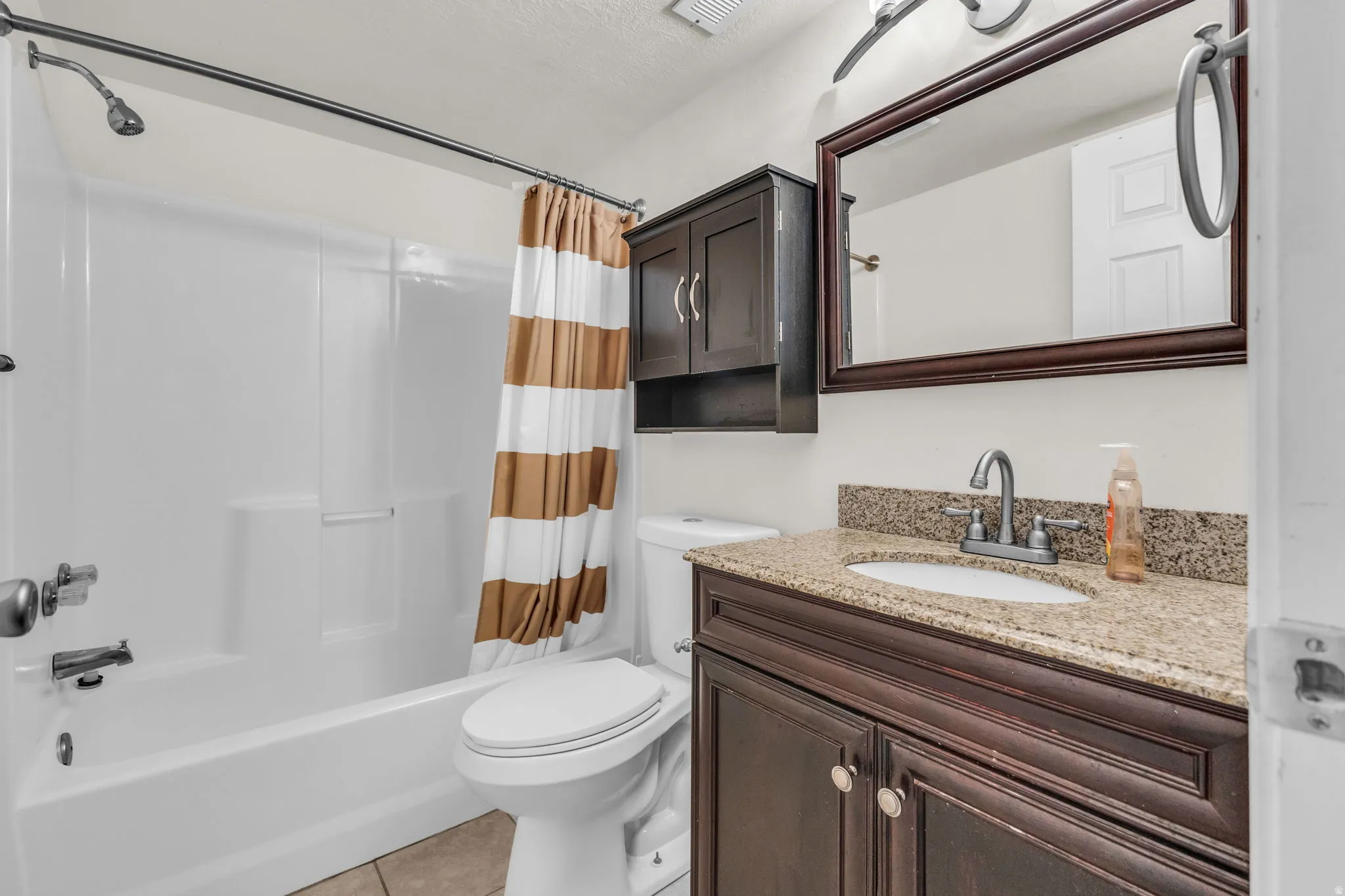 Bathroom featuring a dark wood vanity with a granite-finish countertop and undermount sink, a framed mirror, and a white tub/shower combination