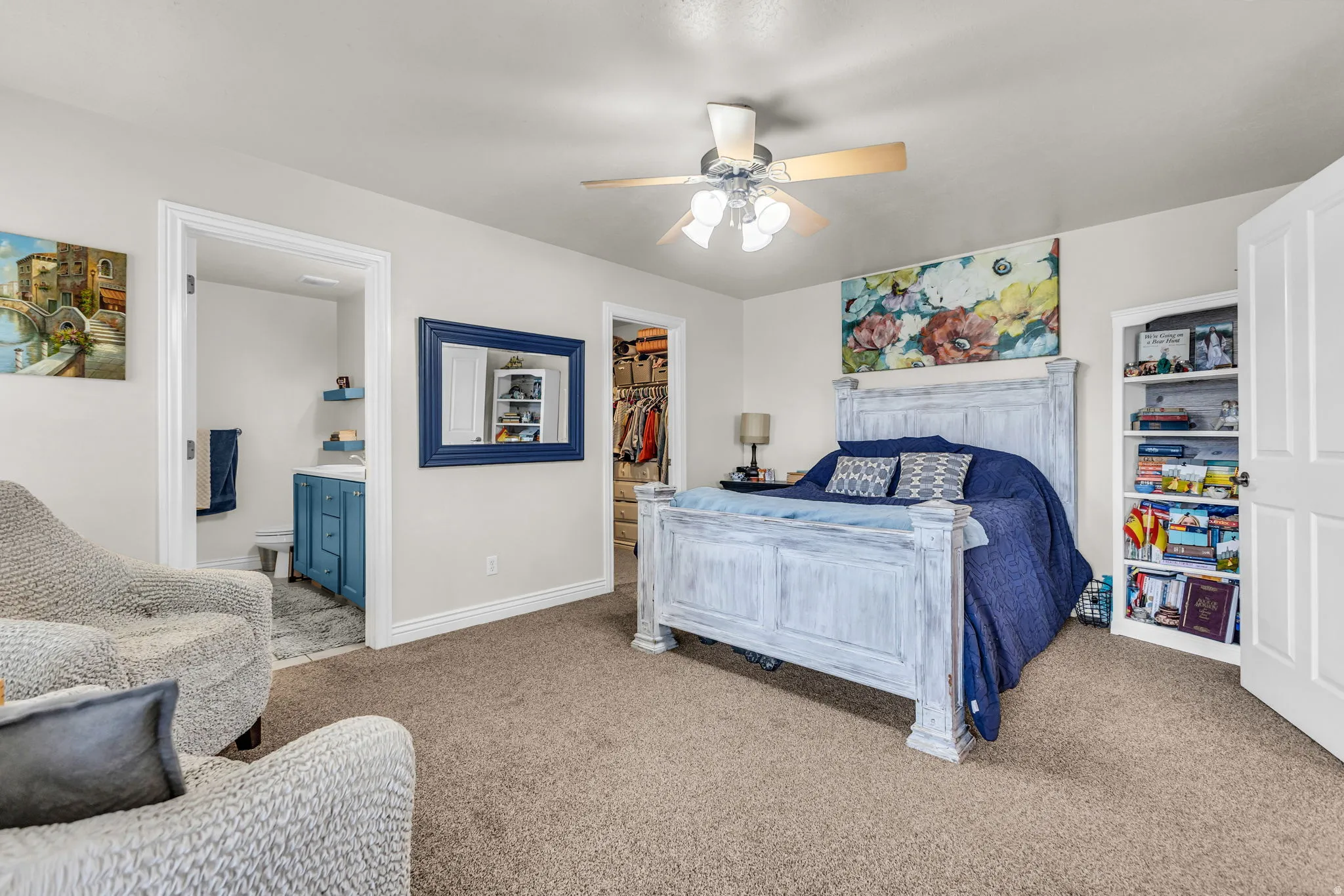 Carpeted bedroom with a ceiling fan, offering direct access to a bathroom with a blue vanity and a walk-in closet
