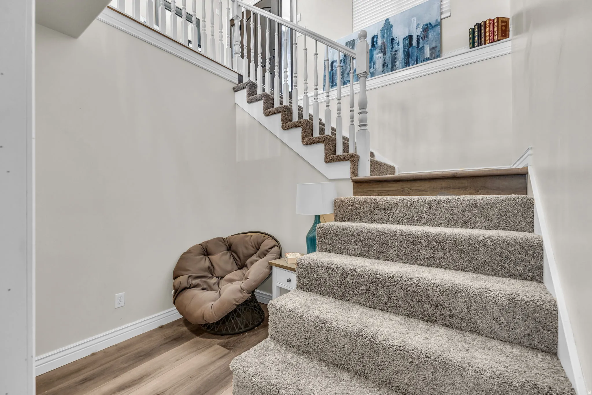 Carpeted staircase with white balusters and wood-finish handrail, featuring wood-finish flooring at the base