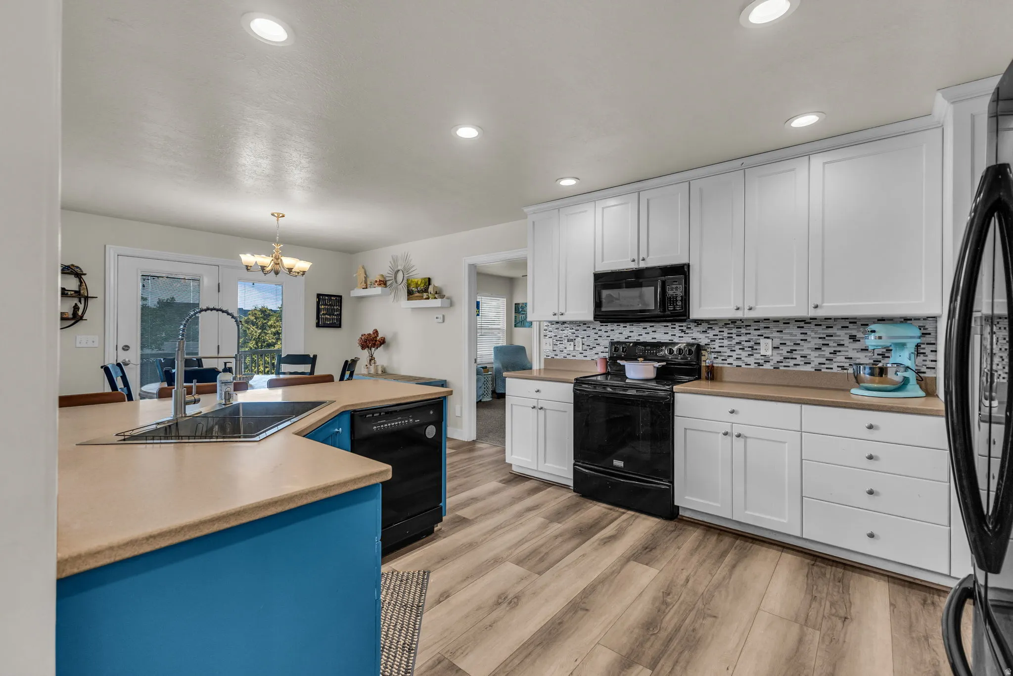 Kitchen featuring wood-finish flooring, white cabinetry, black appliances, a tile backsplash, and an island with a stainless steel sink