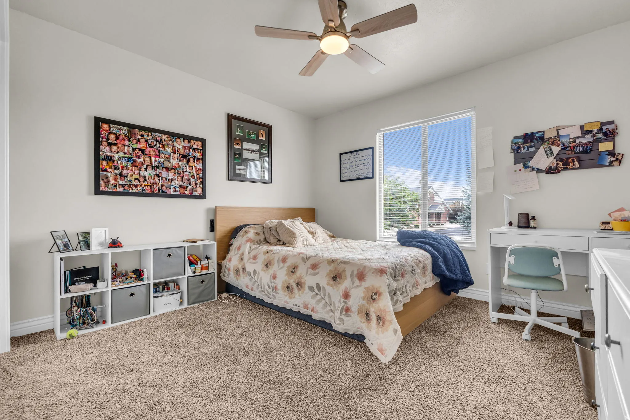 Bright interior space featuring a window with exterior views, light wood-finish ceiling fan, neutral carpet flooring, built-in shelving, and white baseboards