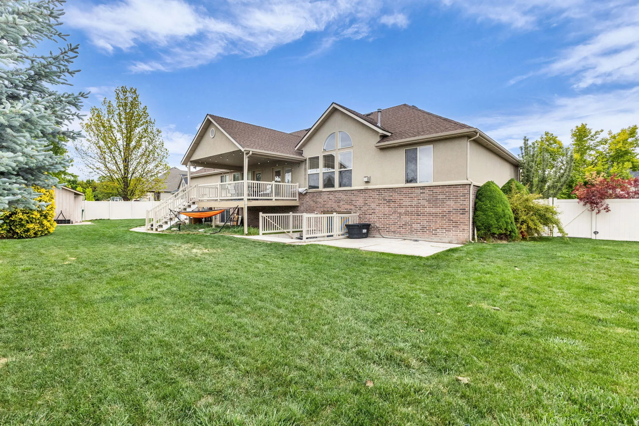 Spacious backyard featuring a manicured lawn, an elevated covered deck with white railings, and a lower patio area